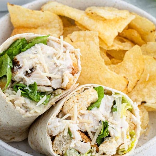 Two chicken Caesar wraps with lettuce, cheese, and croutons, served with a side of potato chips.