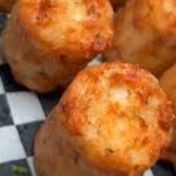 Close-up of golden-brown, crispy tater tots or similar fried appetizers on a checkered paper liner.