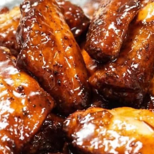 Close-up of glistening, dark brown chicken wings coated in a thick, sweet sauce.