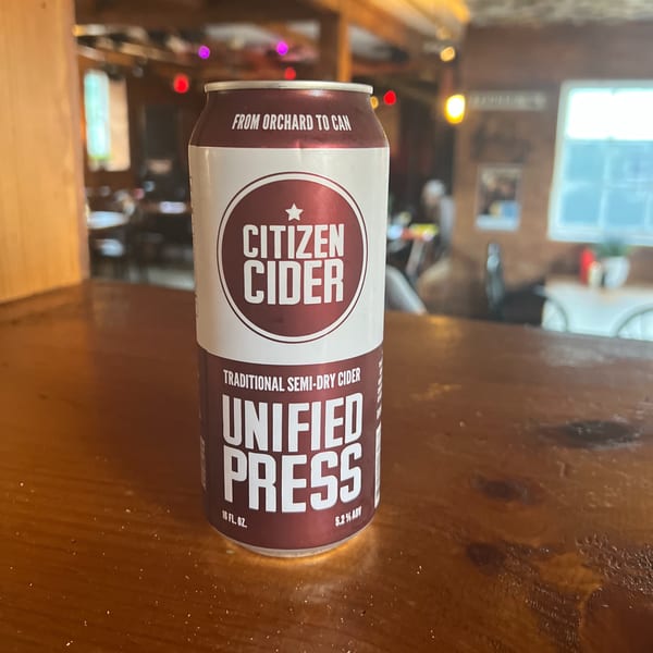 A can of Citizen Cider Unified Press, a traditional semi-dry cider, on a wooden bar top.