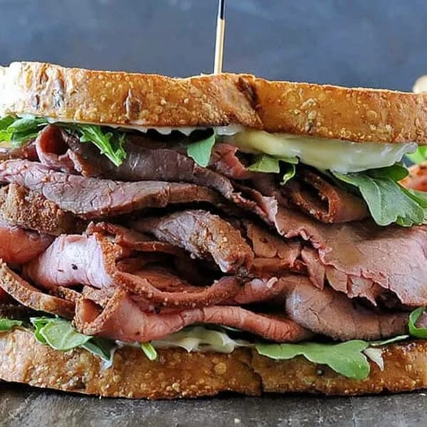 A thick roast beef sandwich on toasted bread with arugula and a creamy sauce.