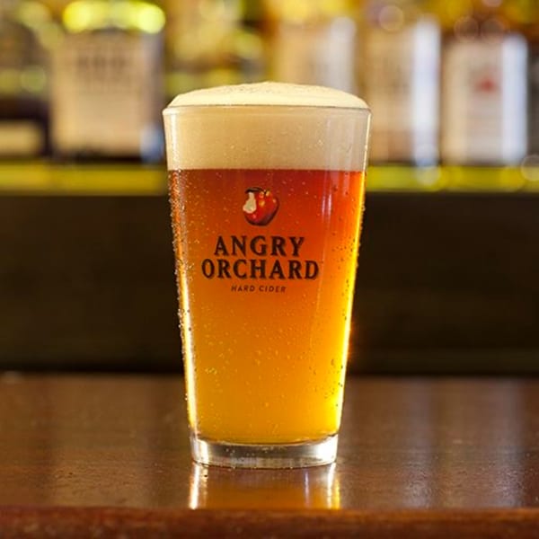 A glass of Angry Orchard Hard Cider with foam on top, condensation, and the logo visible.