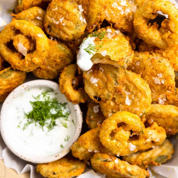 Close-up of golden-brown fried pickles with coarse salt, served with a side of creamy dill dipping sauce.