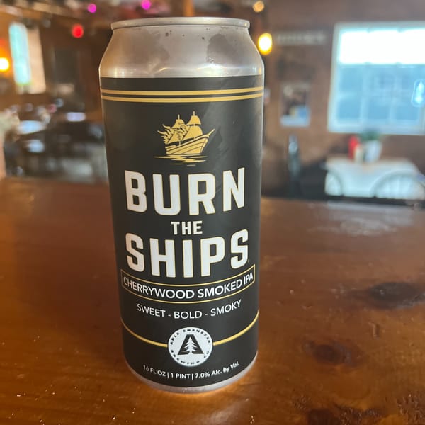 A can of "Burn the Ships Cherrywood Smoked IPA" beer on a wooden bar top at Riley's Place.