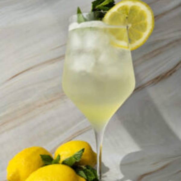 A refreshing lemonade cocktail with ice, a lemon slice, and mint, surrounded by fresh lemons.