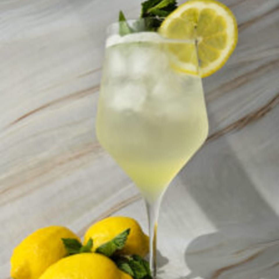 A refreshing lemonade cocktail with ice, a lemon slice, and mint, surrounded by fresh lemons.