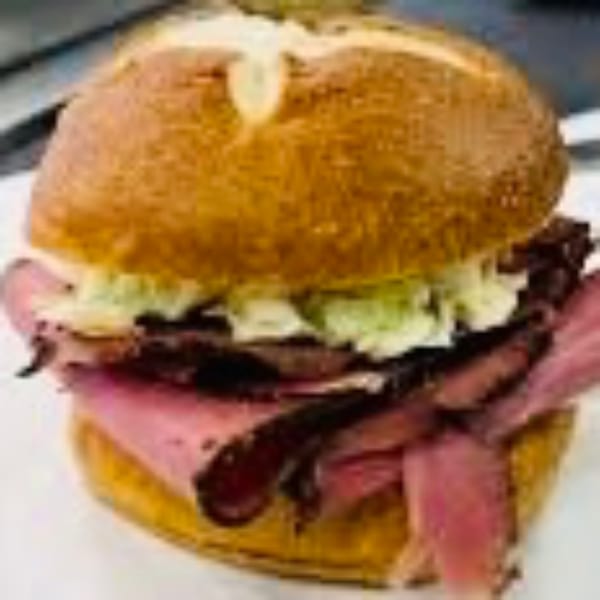 A close-up of a pastrami sandwich on a pretzel bun with coleslaw, from Riley's Place.