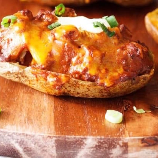 A loaded baked potato with chili, melted cheddar cheese, sour cream, and green onions on a wooden board.