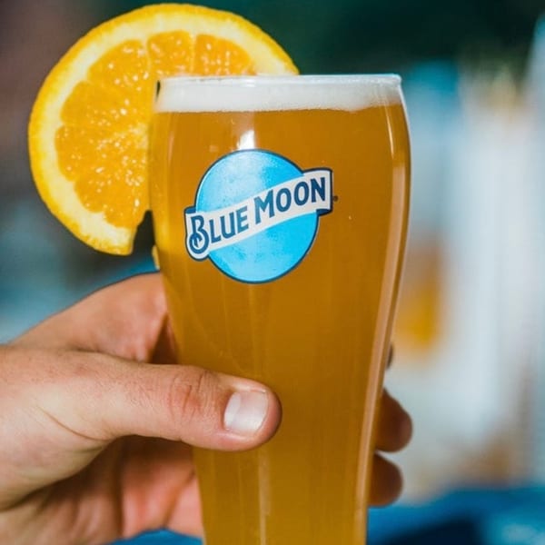 Hand holding a glass of Blue Moon beer with an orange slice on the rim.