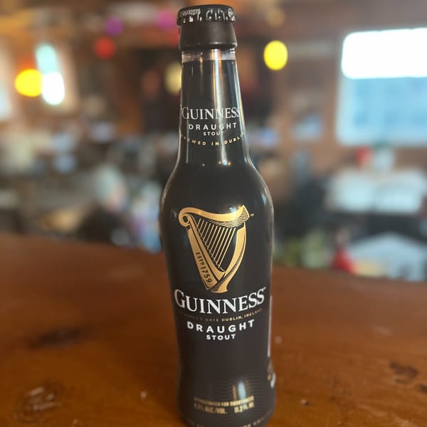 A bottle of Guinness Draught Stout sits on a wooden bar at Riley's Place.