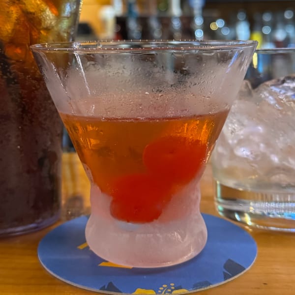 A short, frosted glass of amber liquid with two red cherries, on a blue coaster.