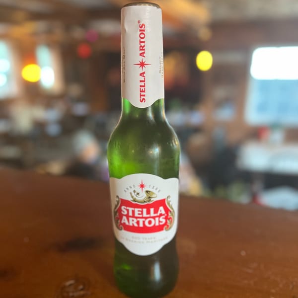 A Stella Artois beer bottle stands on a wooden bar top at Riley's Place.