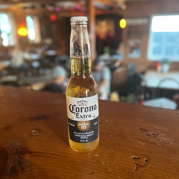 A Corona Extra beer bottle sits on a wooden bar top at Riley's Place.