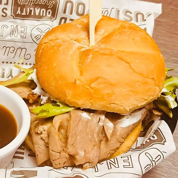A close-up of a hearty roast beef sandwich with lettuce and sauce, served with a side of au jus.