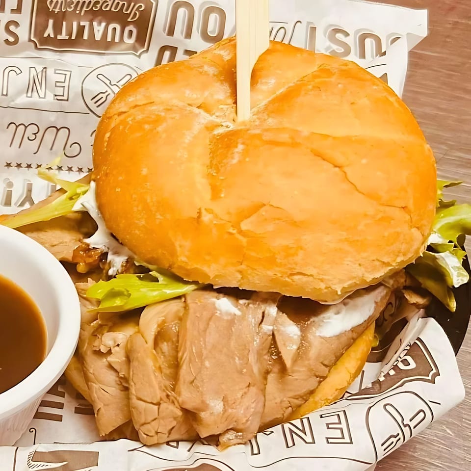 A close-up of a hearty roast beef sandwich with lettuce and sauce, served with a side of au jus.