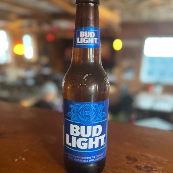 A cold bottle of Bud Light beer on a wooden bar top at Riley's Place.