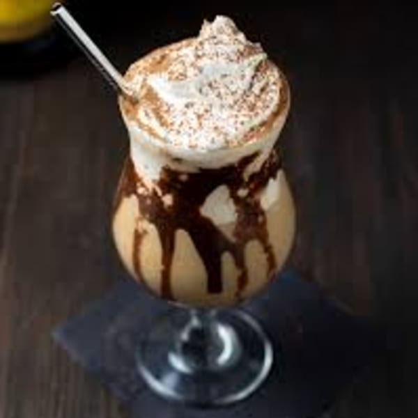 A chocolate milkshake with whipped cream and chocolate drizzle, served in a tall glass with a straw.