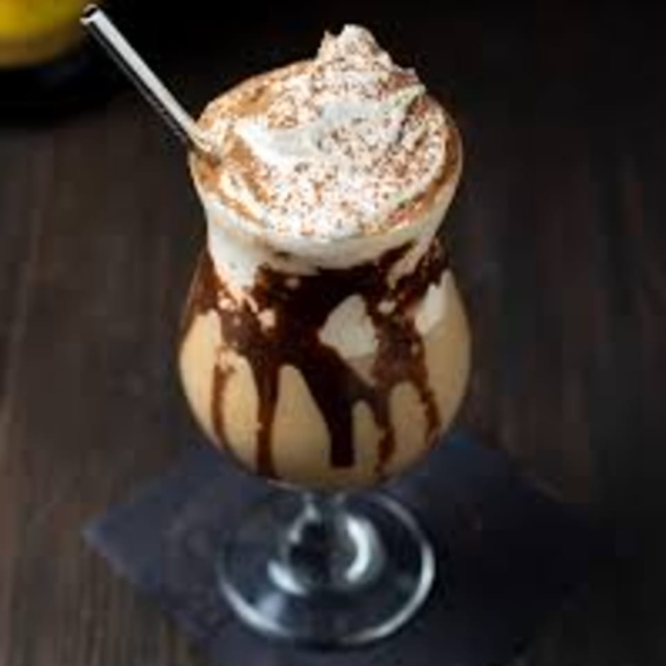 A chocolate milkshake with whipped cream and chocolate drizzle, served in a tall glass with a straw.