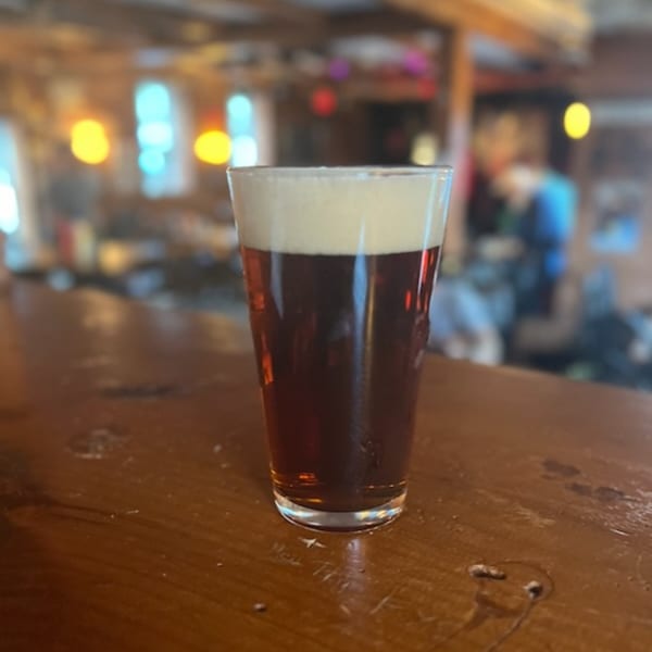 A pint of dark beer with a foamy head sits on a wooden bar at Riley's Place.