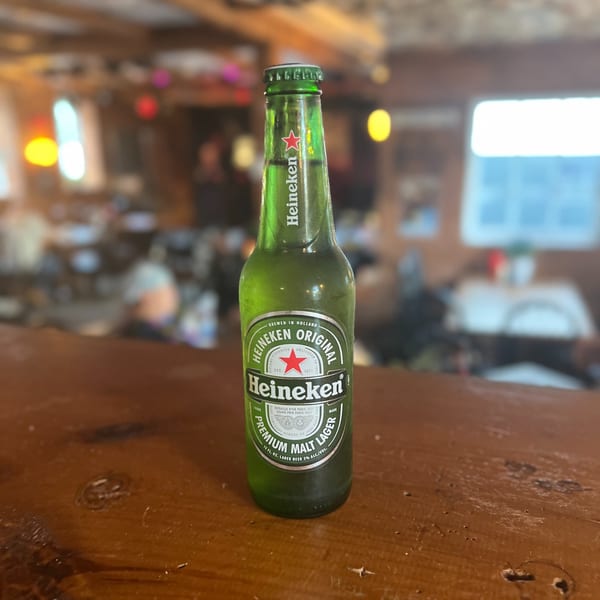 A green Heineken beer bottle sits on a wooden bar top at Riley's Place.
