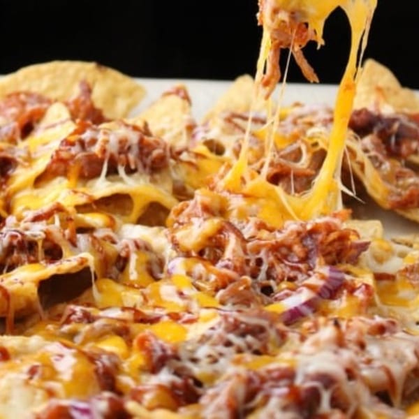 Close-up of cheesy pulled pork nachos with melted cheese stretching from a serving.
